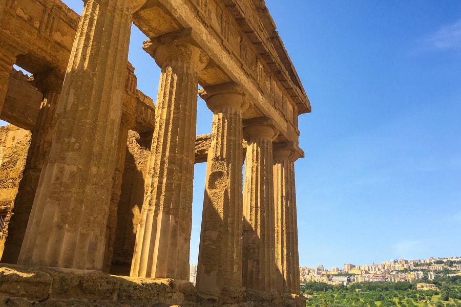 In the foreground, five mustard-coloured columns rise to a pediment while the modern city of Agrigento rises in the distance to the right. 