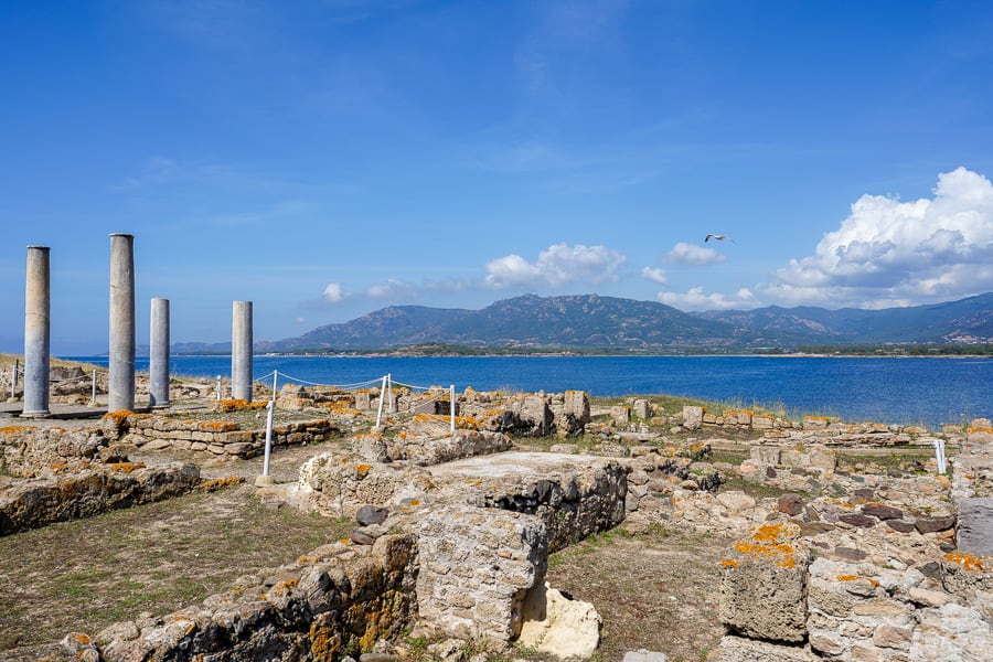 The iconic pillars of Atrio Trestastilo overlook the Tyrrhenian Sea on a sunny day at Nora Roman site - one of many historic things to do in Sardinia.
