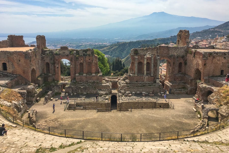 Behind the tiered stone steps of Taormina’s Greek Theatre and semi-circular stage, Mount Etna rises in the distance in dramatic hazy blue. 