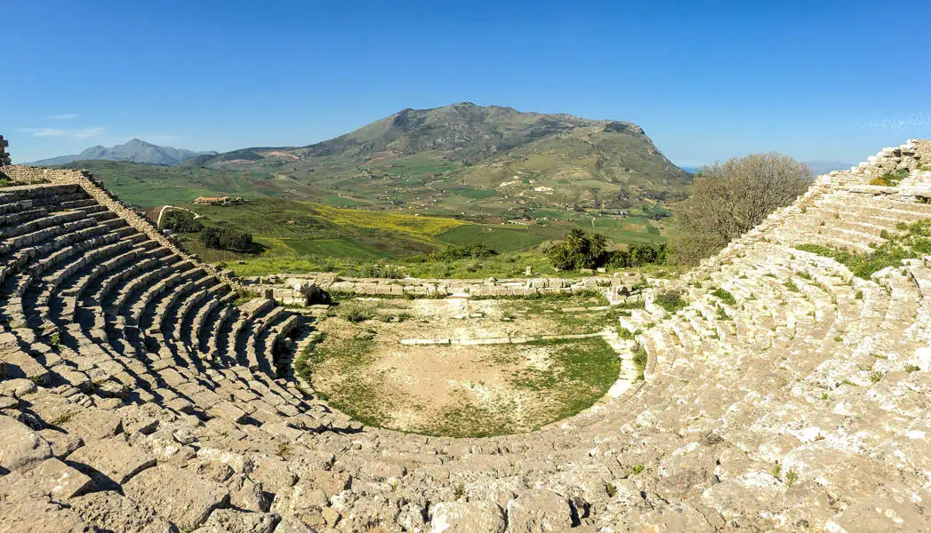 Sweeping views across a green valley to a rocky mountain from the ancient theatre at Segesta in Sicily.