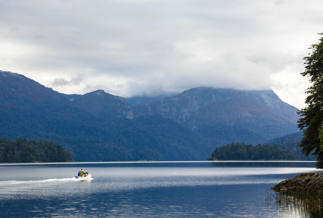 A boat looks small against the mountain backdrop of Lake Espejo on the Seven Lakes Route.