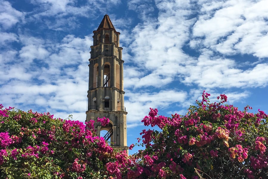 Cuba itinerary 2 weeks: The historic tower of Manaca Iznaga rises behind a hedge of pink flowers.
