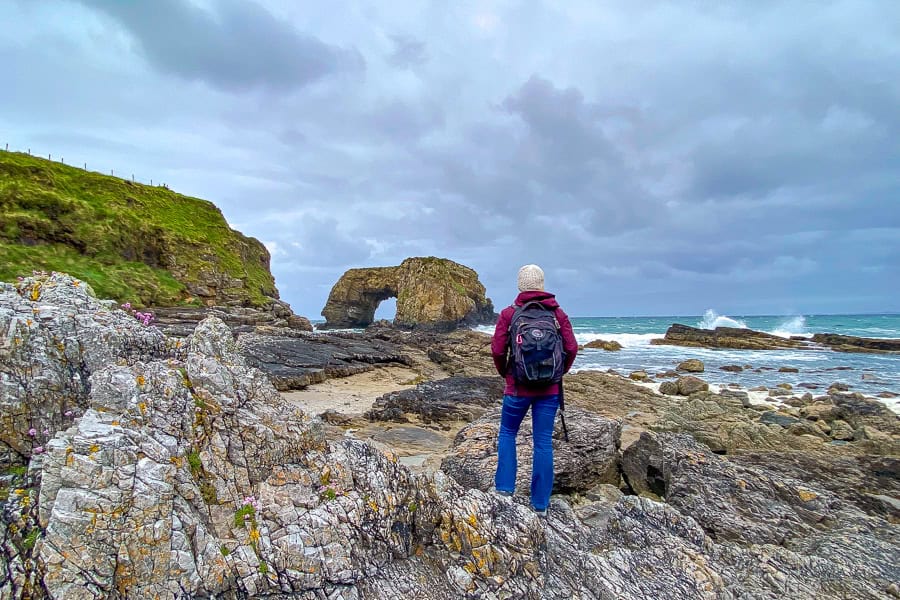 A traveller looks out at the Great Pollet Sea Arch with waves crashing on the rocky shoreline.