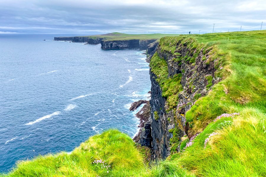 The grassy headland and cliffs along the Loop Head Trail, backed by a foreboding, dark sky, suggest a storm is on the way.
