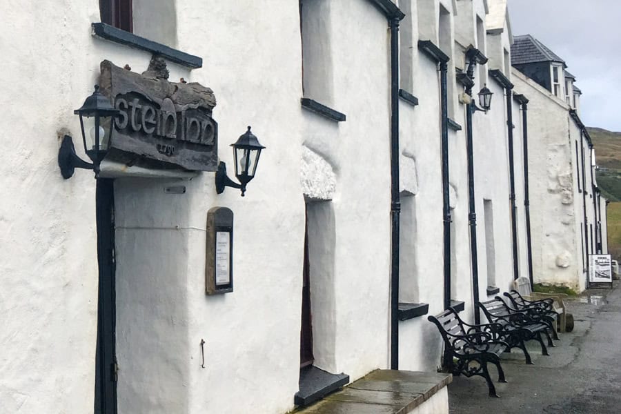 A long white building with black benches in front and a Stein Inn sign, the oldest of Isle of Skye hotels.