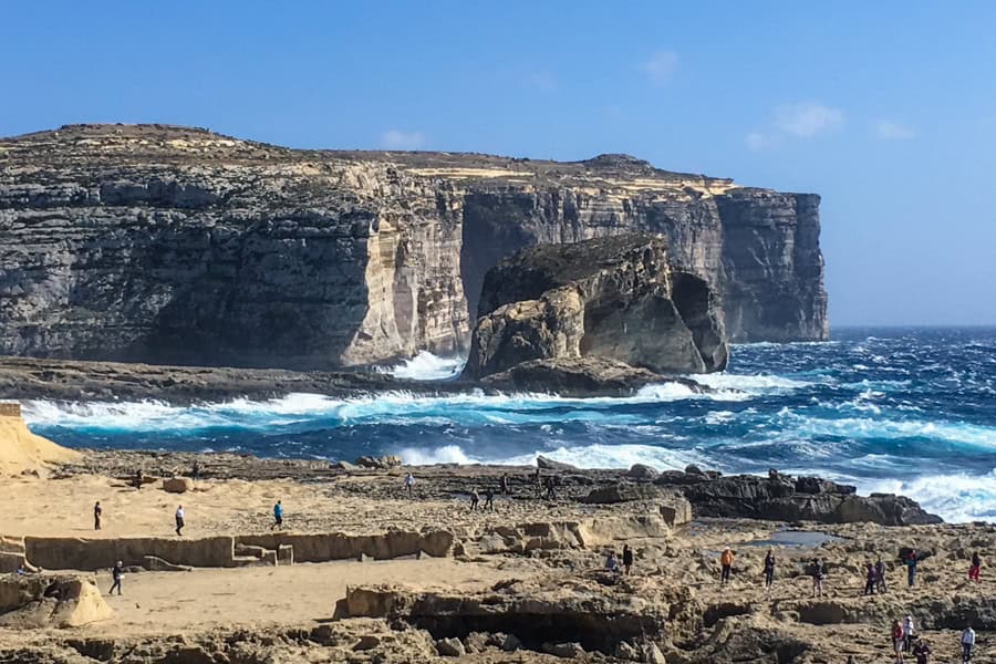 Waves crash on a rocky coastline with cliffs rising in the background.