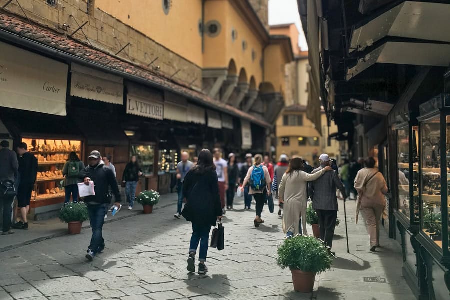 People walking on the Ponte Vecchio in Florence with shops on each side.