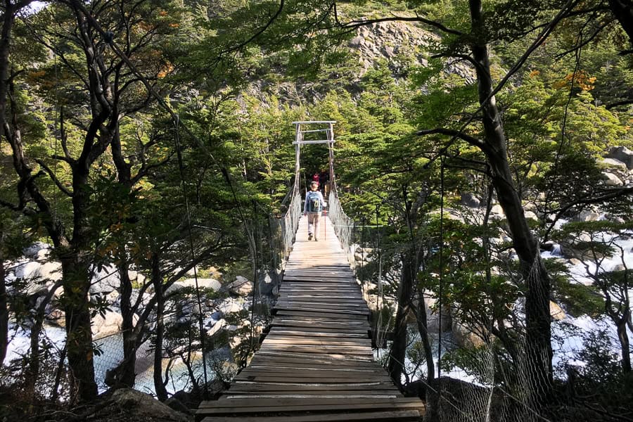 A person crosses a suspension bridge over a river while hiking the W.