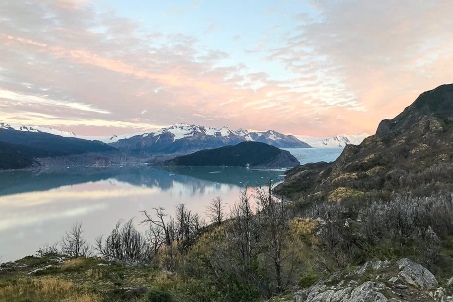 Peach-tinted clouds above a lake with snow-capped mountains in the distance, view from the W trail Patagonia.