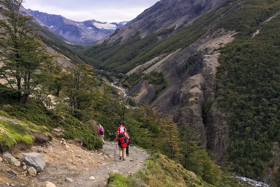 A group of people hike along a trail above a valley with a river through it on the Torres del Paine W Trek.