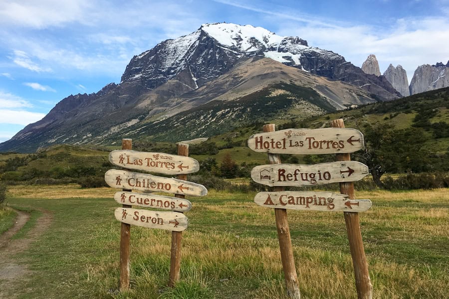 Trekking signs in the foreground with a large, snow-capped mountain in the background.