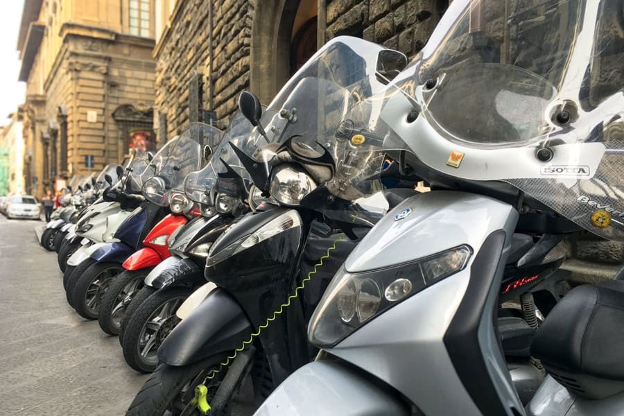 A row of scooters parked in front of stone buildings in Florence.