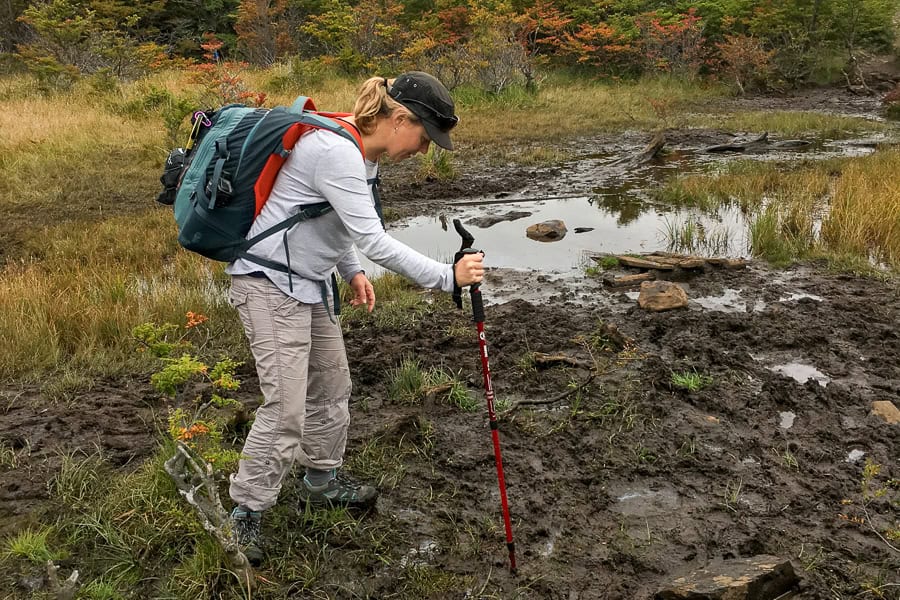 A person tests a muddy patch with a hiking pole while hiking in Torres del Paine.