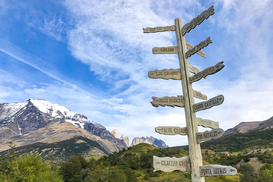 A tall signpost with a mountain behind points to multiple places for those hiking in Torres del Paine.