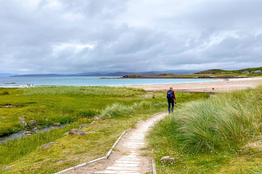 A walkway runs beside a small creek lined with wildflowers behind Mellon Udrigle Beach on the NC500 route.