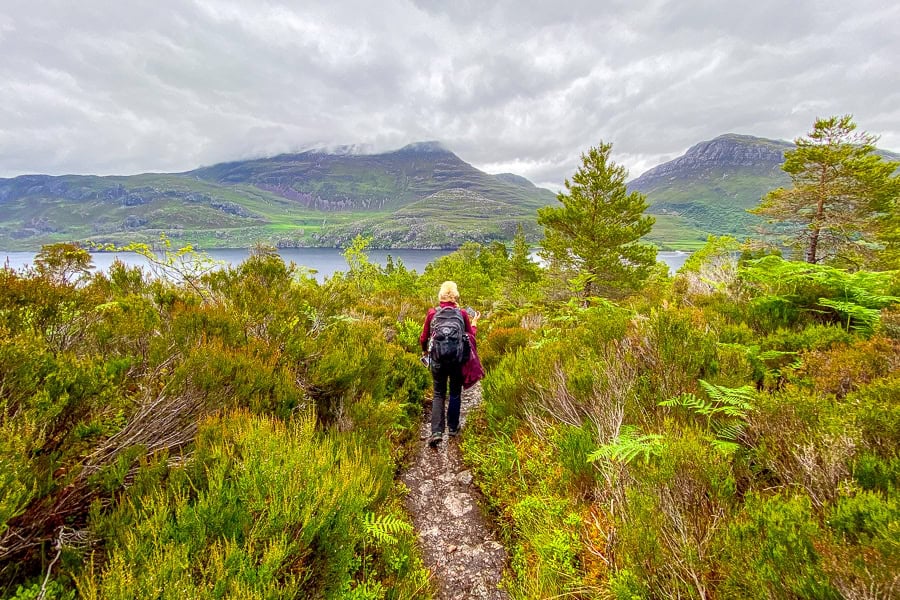 A hiker enjoying sweeping mountain and loch views from Beinn Eighe Trail during a Scotland road trip.