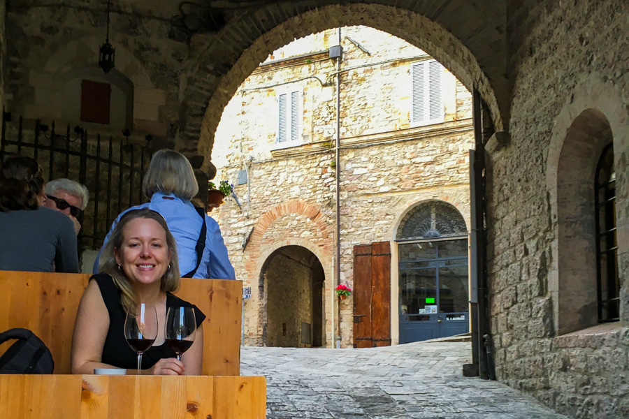 Visitors drinking local wine under medieval archways in Assisi while exploring the hill towns in Italy.