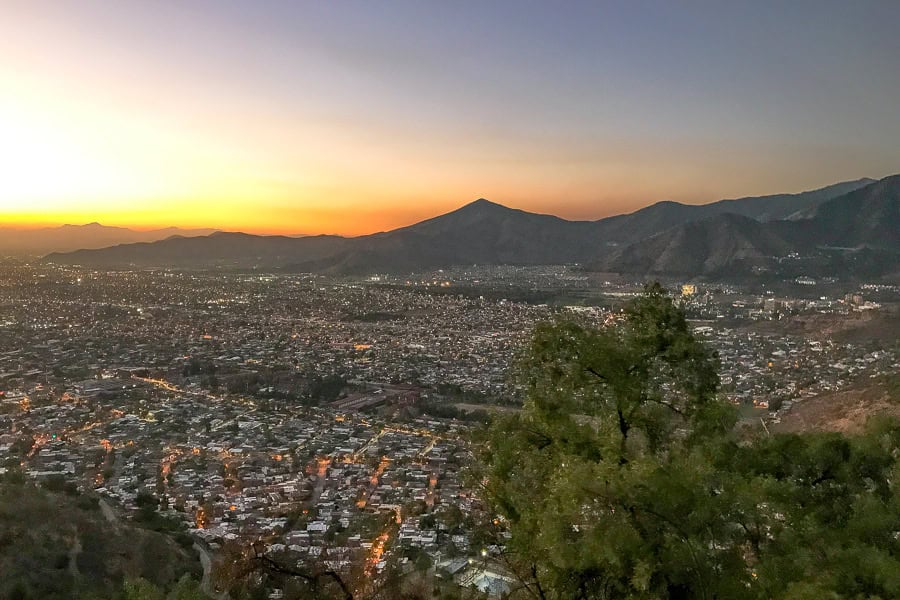 A burnt orange sunset behind mountains and the city from Cerro San Cristobal – one of the cool things to do in Santiago.