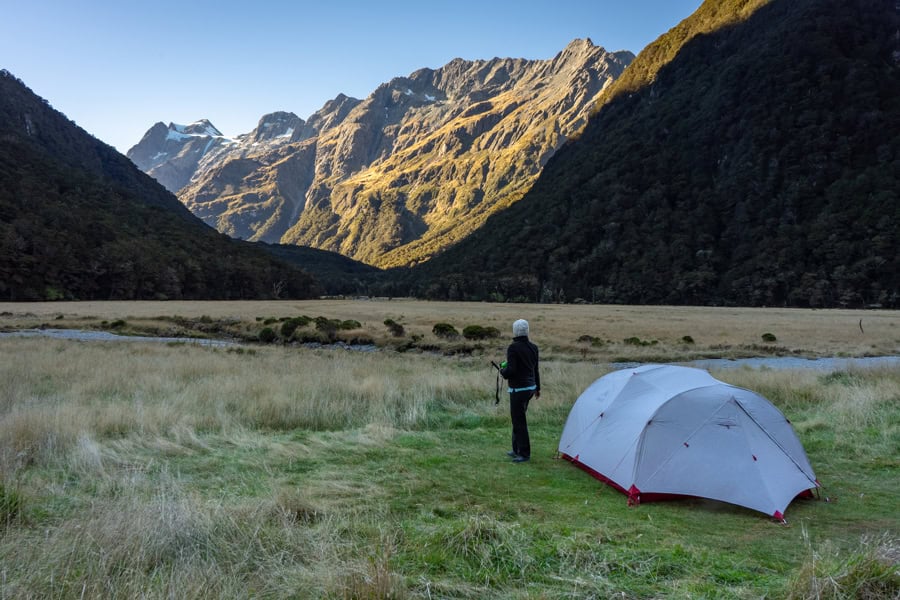 A camper stands beside a tent looking towards mountains on the Routeburn hike.