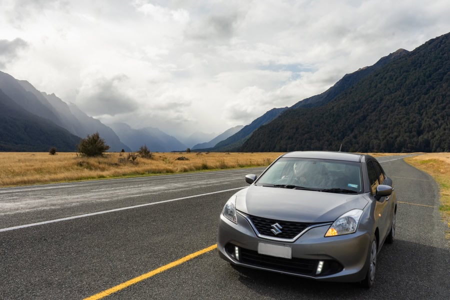 A car parked on the roadside with mountains in the distance.