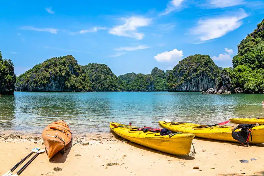 Three kayaks resting on a sandy beach in Bai Tu Long Bay, a great alternative to Halong Bay cruises.