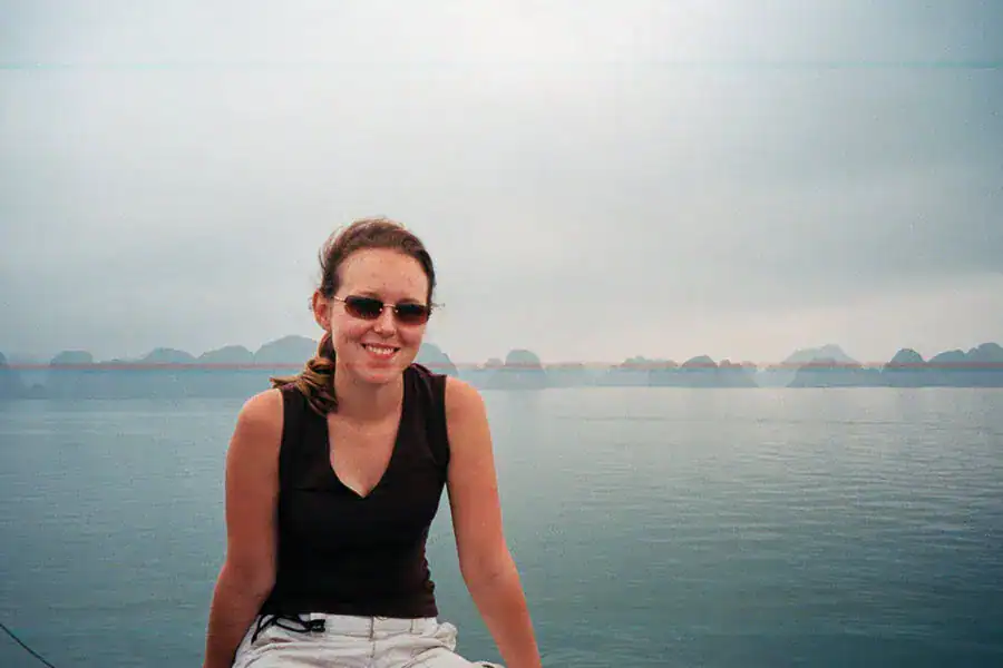 A damaged photo of a person sitting on the deck of a Halong Bay cruise with the famous limestone pinnacles in a misty background.