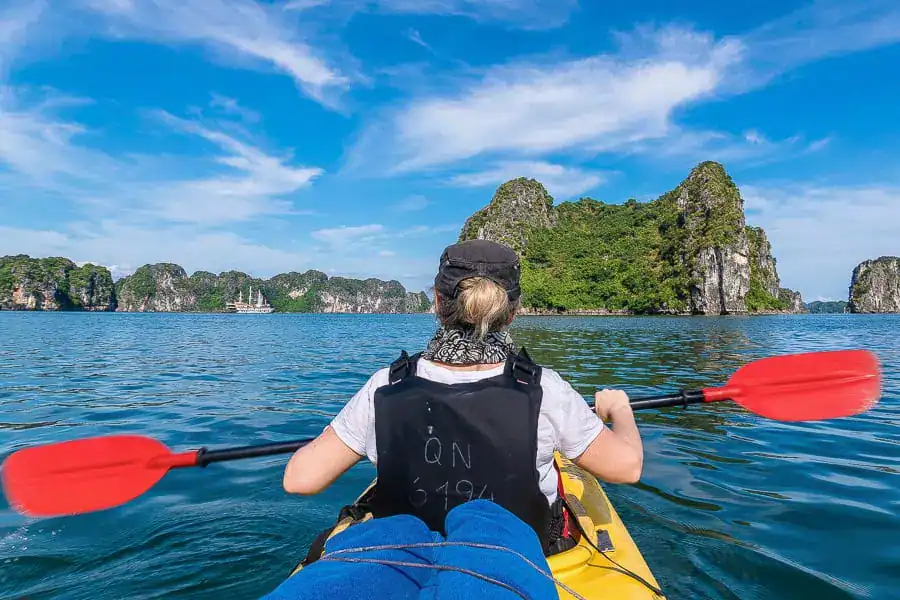 View from behind of a person kayaking in Halong Bay's neighbouring Bai Tu Long Bay on a beautiful sunny day.