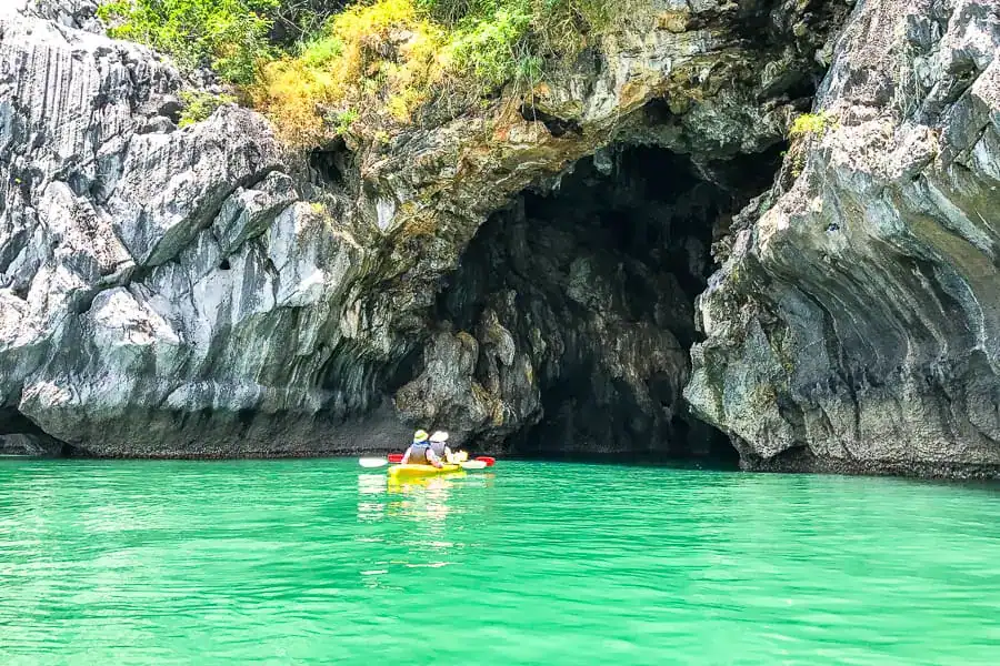 Twin kayak in jade waters enters a cave – kayaking in Halong Bay & Bai Tu Long Bay allows you to see karst islands up close.