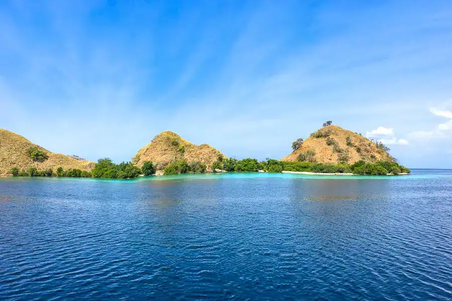 Three small peaks sit in a secluded bay of turquoise water bathed in sunshine on our Komodo diving trip.