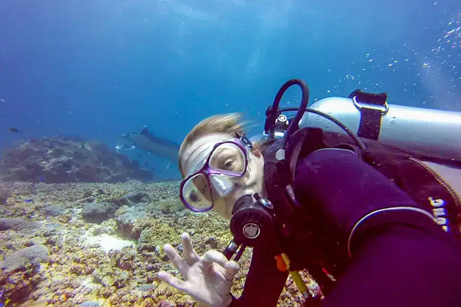 A diver makes an ok sign for the camera while taking a selfie with mantas at manta Point during a Komodo diving trip.
