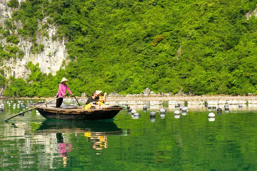 A colourfully dressed local woman rows visitors on a traditional bamboo boat – one of the popular things to do in Halong Bay.