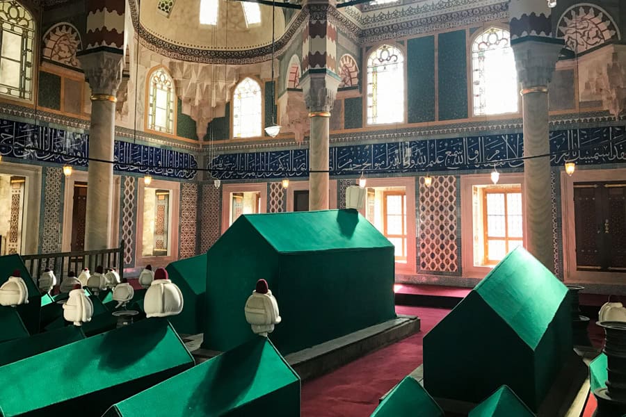 Decorated tiles and columns fill a room with green coffins.