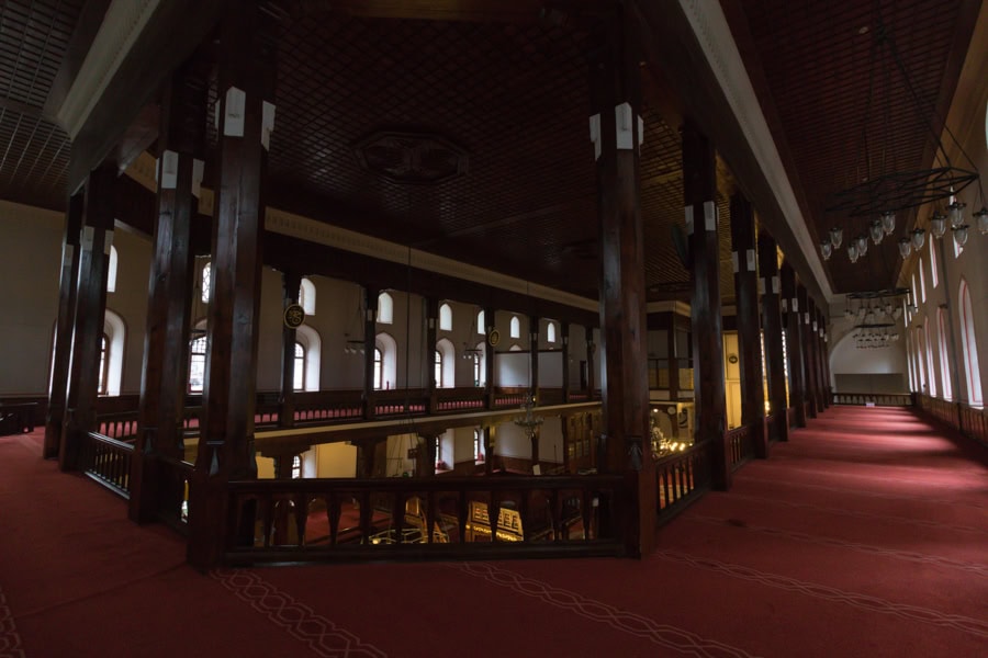A long room with arched windows, dark wood columns and red carpet.