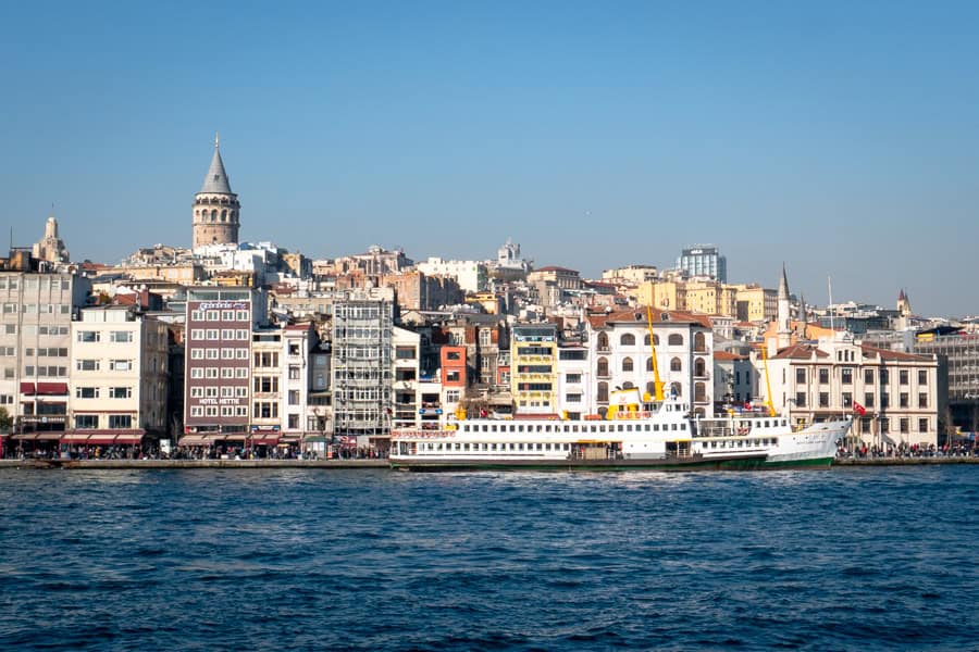 A ferry for getting around Istanbul docked with buildings and Galata Tower rising in the background.