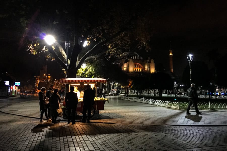 People gather around a street food stall with Hagia Sophia in the background at night on an Istanbul itinerary.