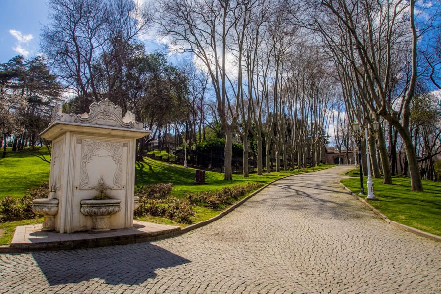 A small fountain on a cobbled path with trees in the background.