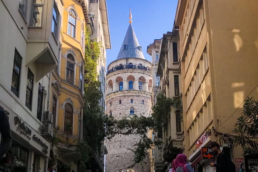 A tall tower with a pointed spire roof with buildings on both sides.
