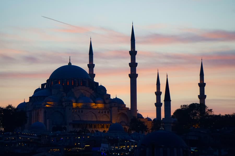 Istanbul itinerary: The domes and towers of the Blue Mosque at twilight with a plane flying above.