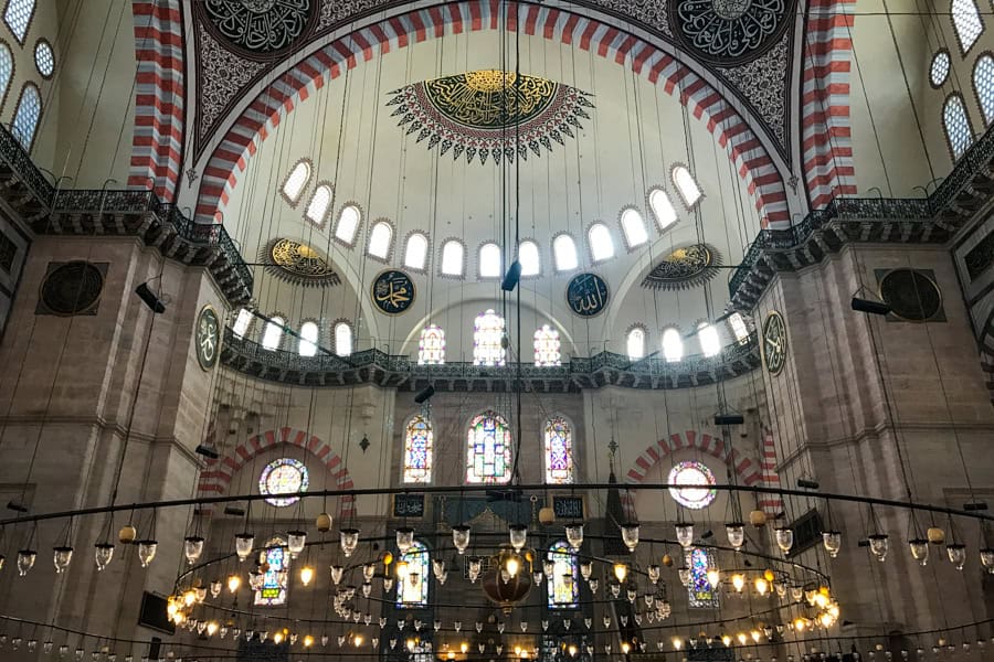 The ornate interior of Süleymaniye Mosque with high arches, domes and many windows.