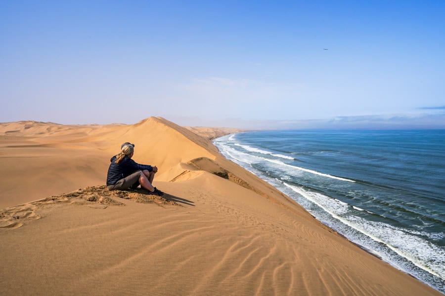 Two people sitting on a sand dune overlooking the sea – the type of quiet moment to enjoy while travelling with your partner.