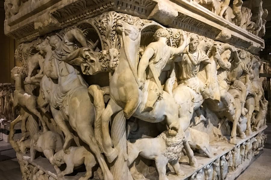 A highly carved sarcophagus with people riding horses.