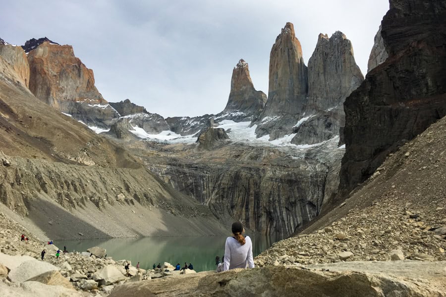 A person sits above a lake at the foot of three peaks at Base Torres Lookout on the W Trek in Patagonia.