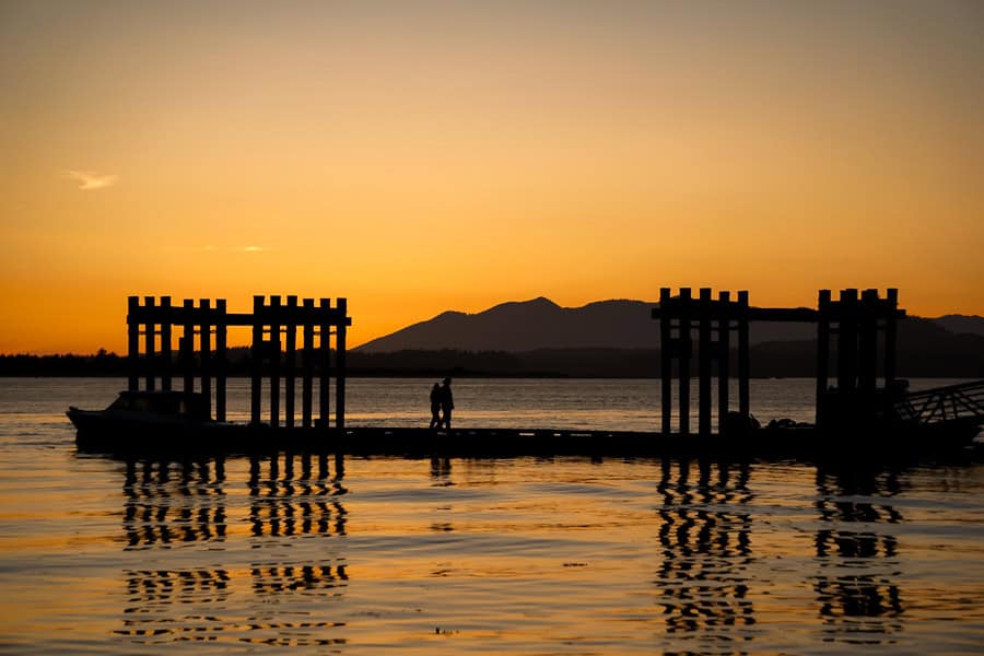 Silhouette of a wharf reflected in the bay at sunset in Tofino, one of the most popular places to visit on Vancouver Island.