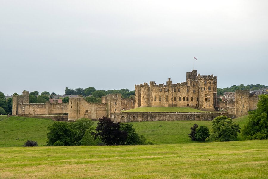 Sweeping views across parkland towards imposing Alnwick castle on a cloudy day – a must stop on a Northumberland itinerary.