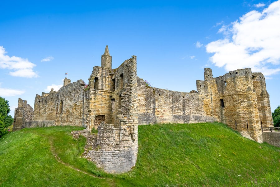 The well-preserved walls of Warkworth Castle circled by a grassy moat - a worthwhile stop on the Northumberland 250 route.