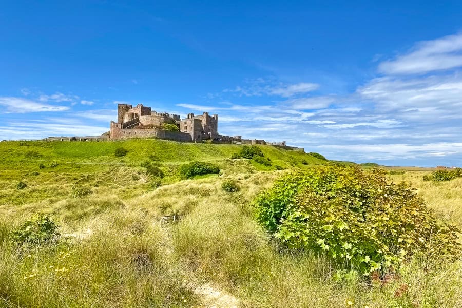 View across grassy dunes towards Bamburgh Castle, one of the highlights of our Northumberland 250 road trip itinerary.