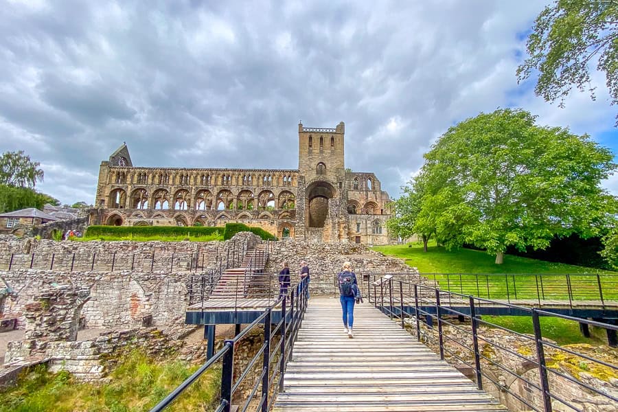 A woman takes the walkway towards the looming remains of Jedburgh Abbey, worth a detour from our Northumberland road trip.