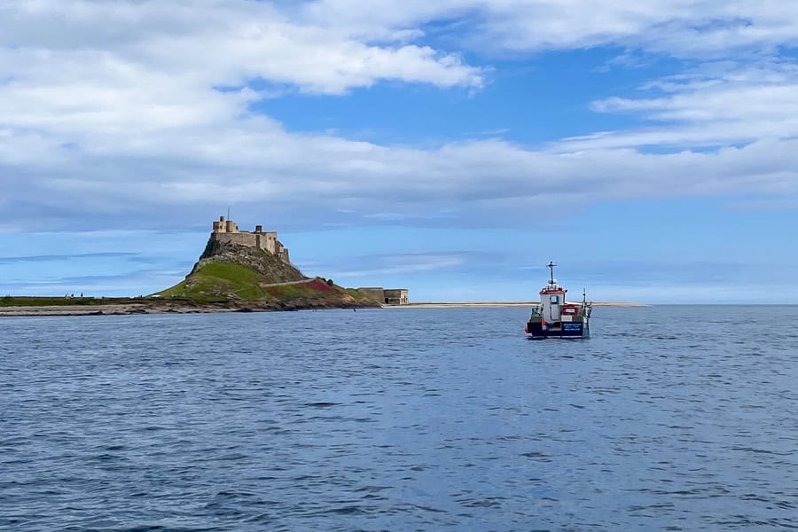 A boat travels towards Holy Island on calm seas with Lindisfarne Castle in the distance.