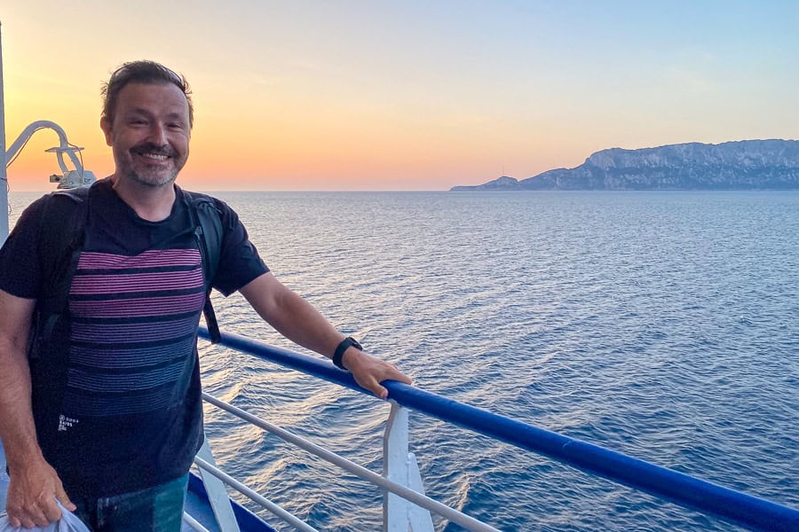 Passenger on deck of the ferry to Sardinia from Civitavecchia with an orange sunrise and hint of land in the background.