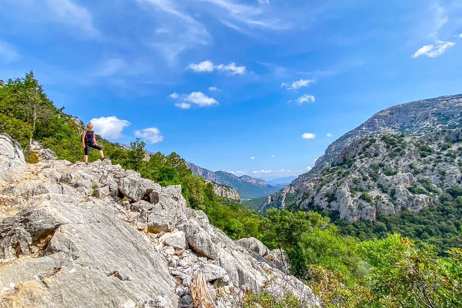 A hiker standing on rocks overlooking a wide, rocky valley on the Tiscali Hike while visiting Sardinia.